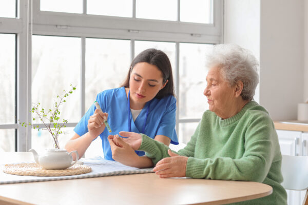 A home health aide checks an elderly patient's blood sugar in her living room.