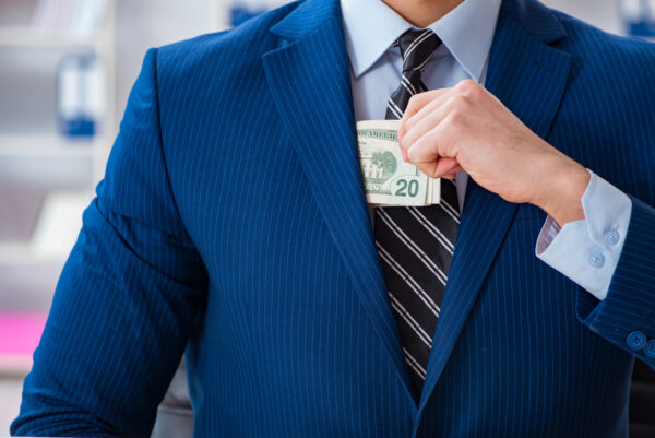 Businessman tucks extra profits from wage theft into his suit pocket.